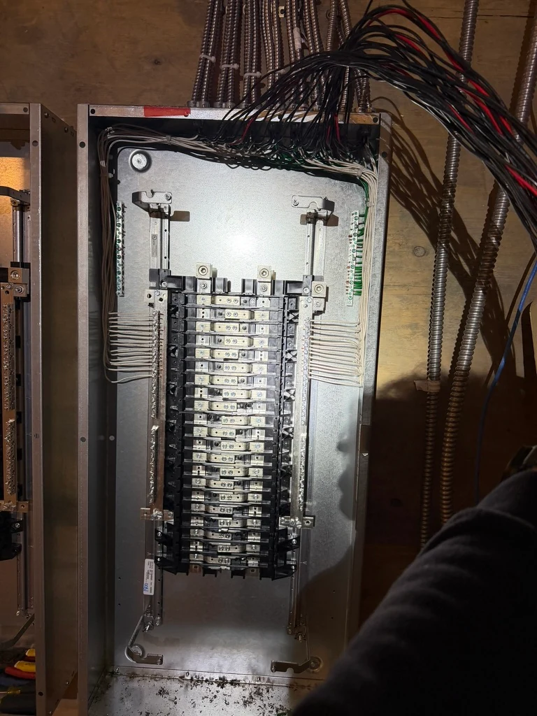 Open electrical panel during wiring work with conductors routed across the top