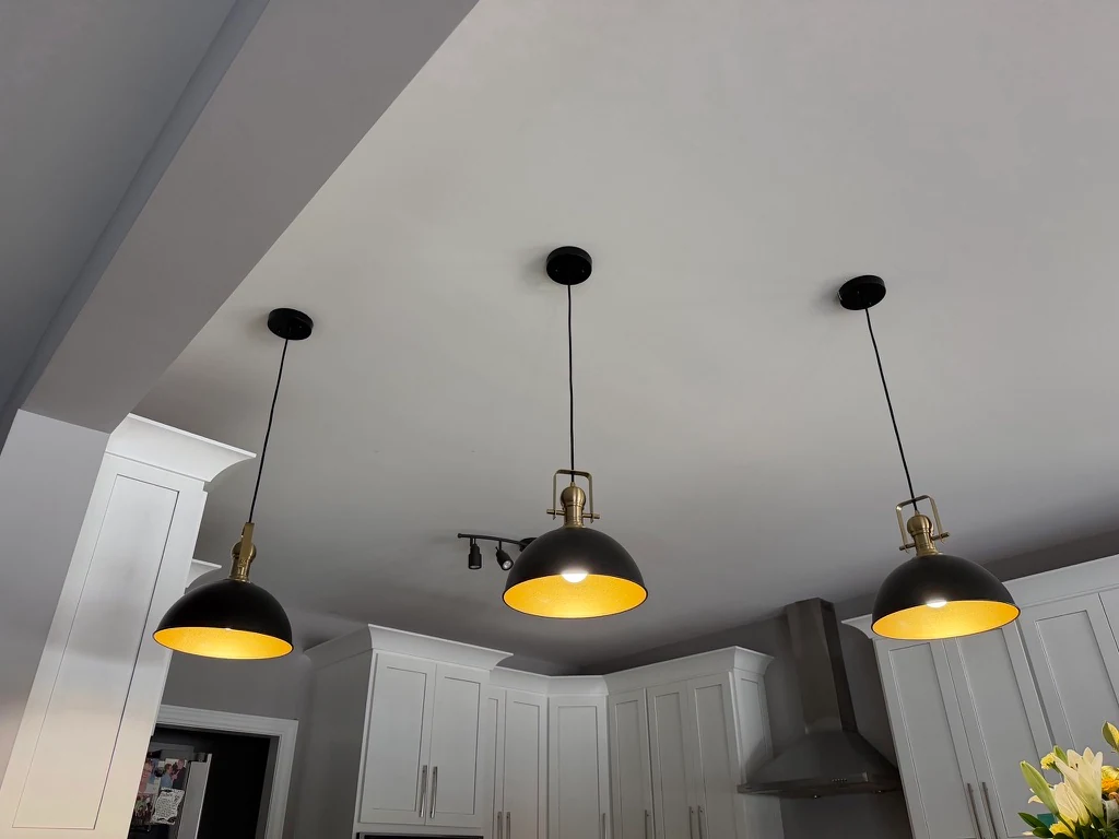 Three black and brass pendant lights illuminated above a white kitchen